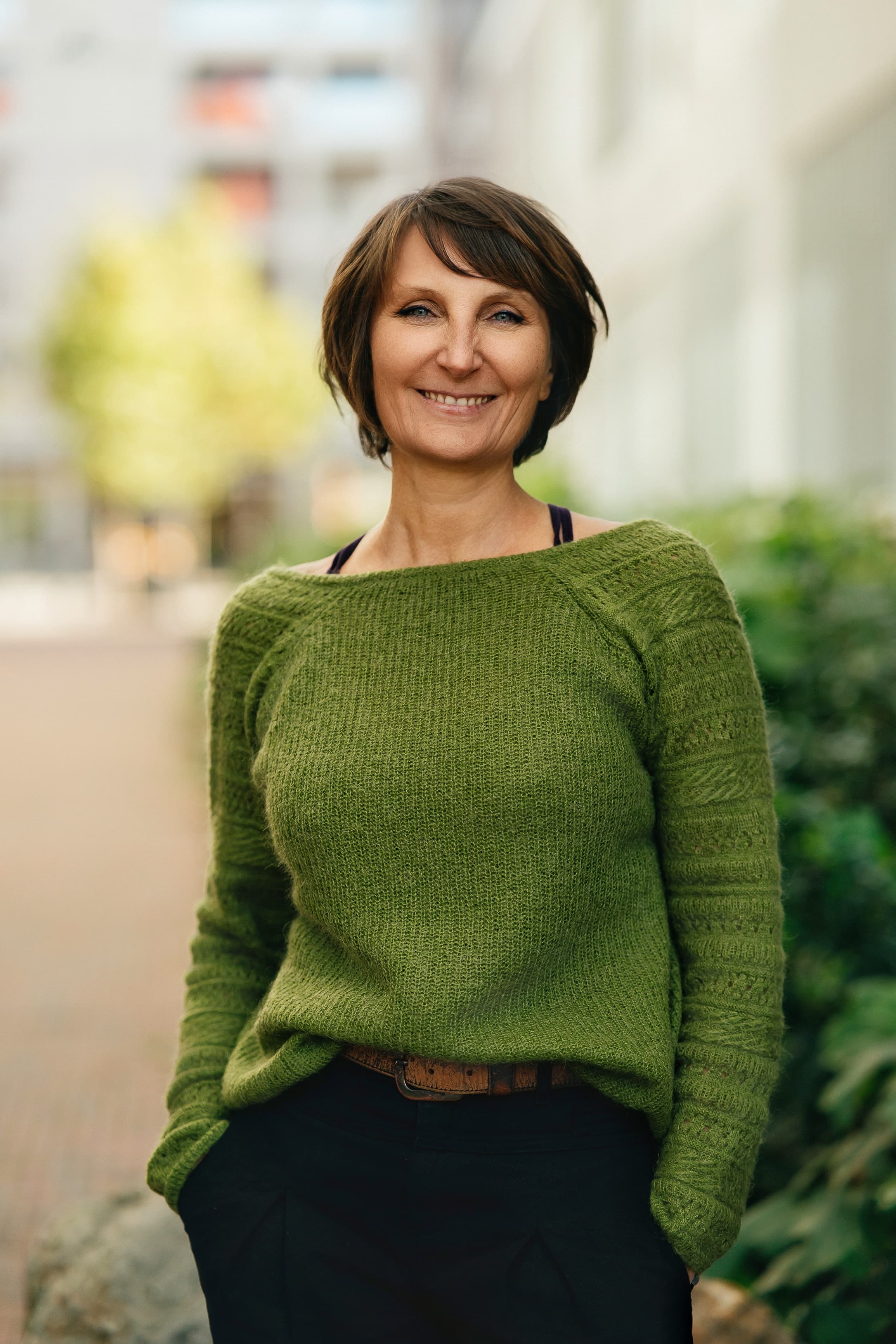 photo de Nathalie Ranno rédactrice indépendante à Rennes, debout mains dans les poches, sourire, pull vert, pantalon noir