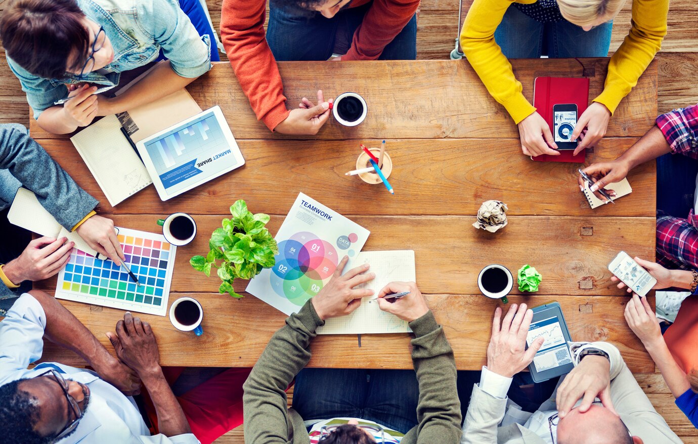 photo de personnes qui travaillent autour d'une table en bois :pot à crayons, boulettes de papier, colorimétrie